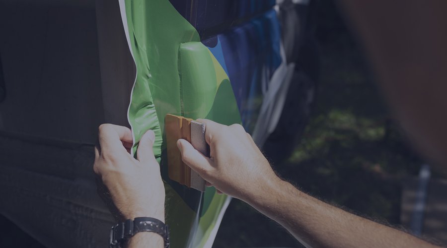 Man applying a green, yellow, and blue coloured car wrap to a vehicle.