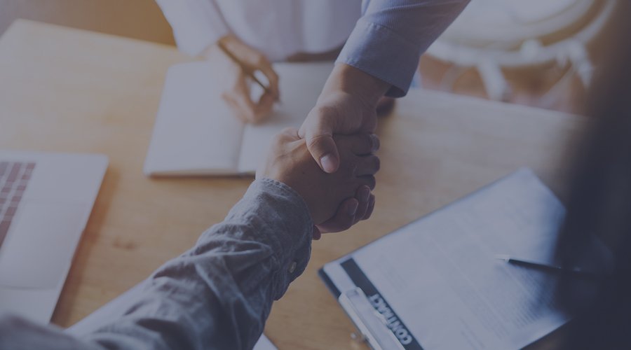 Two people shaking hands after signing a contract.